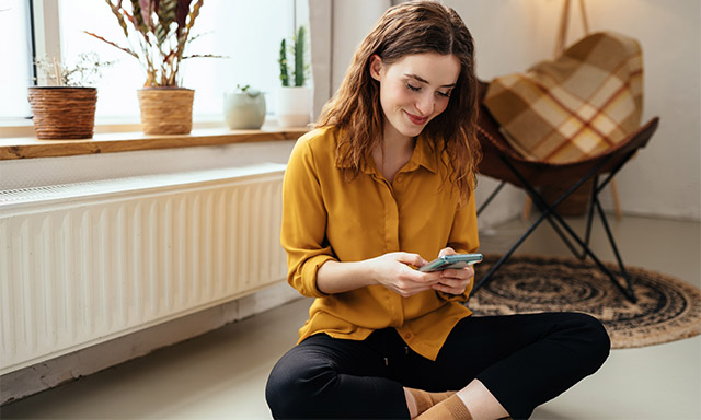 Junge Frau mit Handy sitzt auf Fußboden
