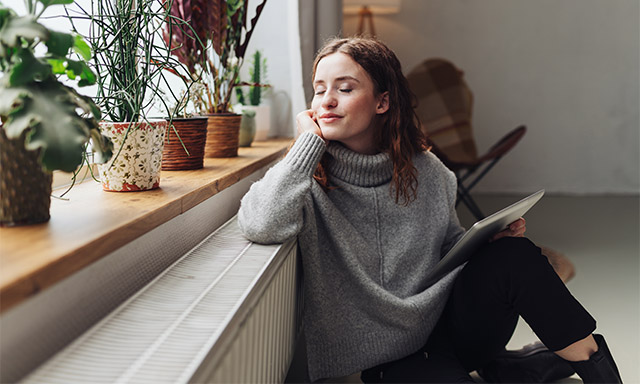 Frau lehnt an Heizung mit Tablet in der Hand